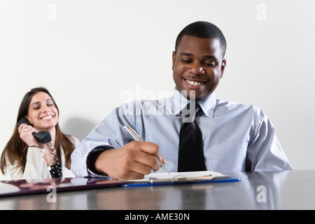 Business-Mann im Vordergrund mit Business-Frau mit Telefon im Hintergrund. Stockfoto