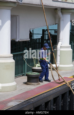 Ein Matrose auf einem bereitet der Kowloon Seite Pier von der Star Ferry, ein Liegeplatz Seil an einem Kollegen auf einer Fähre zu werfen, wie es geht Stockfoto