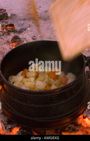 Kochen auf offenem Feuer einen kleinen Kessel auf eine Outdoor-Holz-Feuer-Hand rühren die Brühe Stockfoto