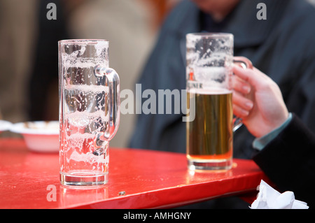 leere deutsches Bierglas auf einem roten Café im freien Tisch neben Womans Hand, die halb vollen Glas Berlin Deutschland Stockfoto