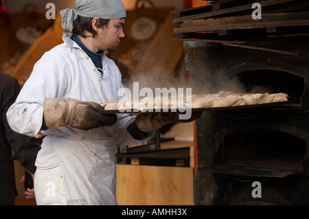 Baker entfernen Tablett mit Brot mit Dampf steigt aus einem Outdoor-Holz Backofen auf einen Stand auf dem Weihnachtsmarkt Berlin Stockfoto