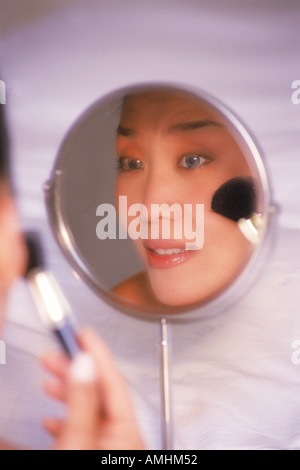 Asian woman applying make up using brush and small mirror Stockfoto