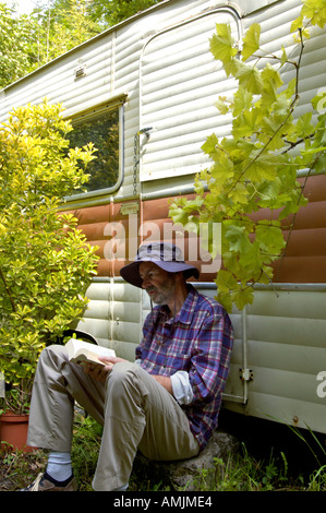 Herr PR Mann sitzt vor einem alten Wohnwagen, ein Buch zu lesen Stockfoto