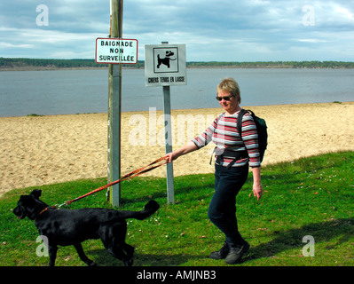 Herr Frau gehen für einen Spaziergang mit dem Hund am Strand eines Sees mit Verbotsschilder für Hunde Stockfoto