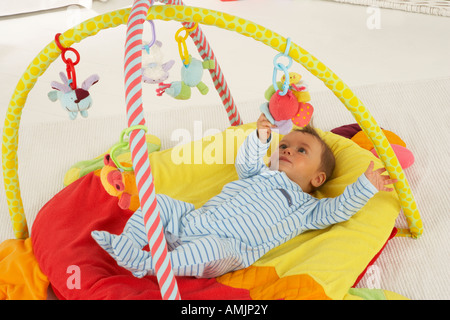 Ein Baby liegt auf dem Rücken auf eine Spielmatte in einem Kindergarten und spielt mit einem mobilen Stockfoto