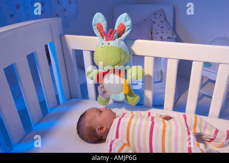 Ein Baby liegt auf dem Rücken in ein Kinderbett in einem Kindergarten und blickt auf eine Nacht Licht Spielzeug Stockfoto