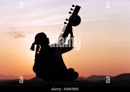 Indischen Mann spielt eine Sitar auf Felsen bei Sonnenuntergang. Indien Stockfoto