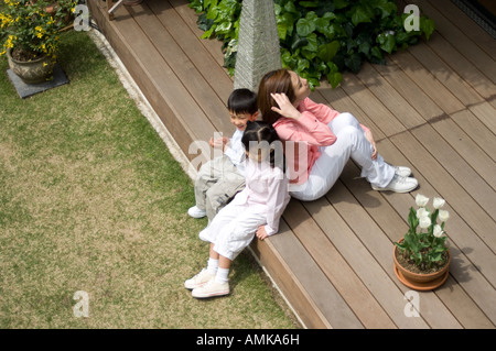 Mutter und Kinder sitzen auf Holzterrasse Stockfoto