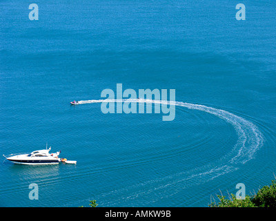 Ansicht eines waterskier durch eine Rippe (Rigid Inflatable Boat) vorbei an einem Verankerten motor yacht an einem sonnigen Sommer an der Küste von South Devon, Großbritannien gezogen wird Stockfoto