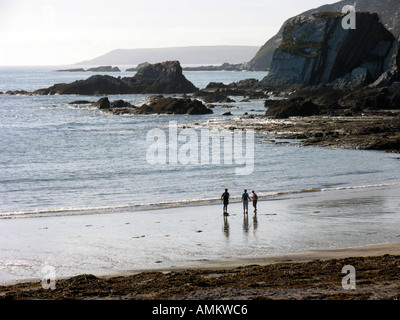 Drei silhouetted Zahlen über Ayrmer Cove Beach mit felsigen Klippen und einen glitzernden Meer in silbrig, am späten Nachmittag Sonne. South Devon, Großbritannien Stockfoto