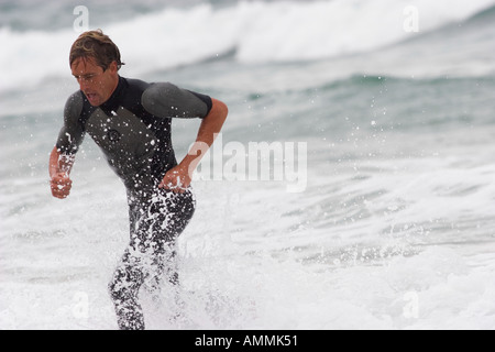 Surfer, die während eines Ironman-Wettbewerbs durch die Wellen laufen Stockfoto