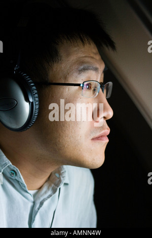 Young Korean American Mann Passagier mit Kopfhörer auf und Suche aus dem Fenster ein Passagierflugzeug Stockfoto