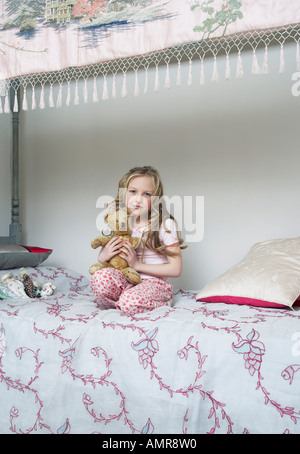 Mädchen auf dem Bett sitzend, hält Teddybär Stockfoto