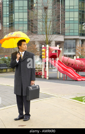 Geschäftsmann mit Kindes Regenschirm auf Spielplatz Stockfoto