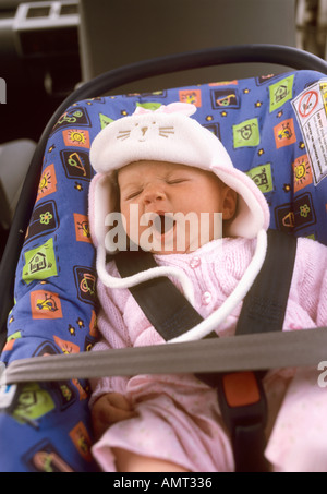 Babymädchen sitzen in einem Autositz Gähnen Stockfoto