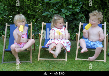 Zwei junge Mädchen und ein Junge Lutscher zu essen, während draußen auf Liegestühlen Stockfoto