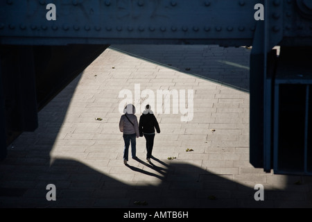 Fußgänger gehen Sie unter Hungerford Eisenbahnbrücke auf der Jubiläums-Gehweg inmitten herbstlichen Morgen Schatten, London, England. Stockfoto