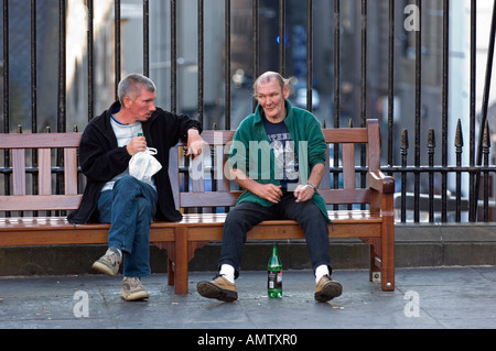 Zwei Erwachsene Männer sitzen auf einer Bank sprechen und trinken Stockfoto