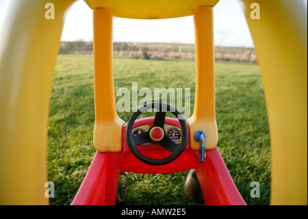 rote und gelbe Kinder Spielzeug Auto zeigen Cockpit mit Lenkrad und große Rasenfläche Garten bietet Exemplar fahren Stockfoto