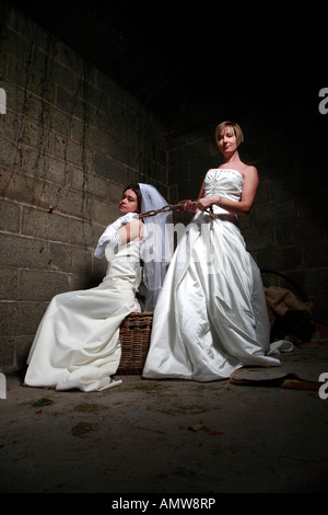 Zwei Bräute kämpfen in einer alten Scheune eine Braut hat eine Kette um den anderen Bräute Hals und zieht sie zurück Stockfoto