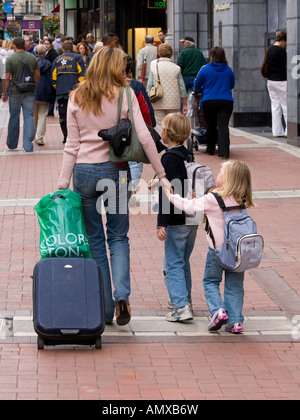 Mutter mit Kindern Hand in Hand beim gehen auf der Straße mit ihrem Gepäck Stockfoto