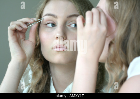 Reflexion der jungen Frau mit Augenbrauen Pinzette im Spiegel Stockfoto