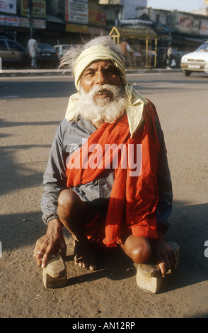 Älterer Mann hocken auf dem Boden halten Holzklötze, die er verwendet, um ihm zu helfen, zu Fuß. Indien Stockfoto
