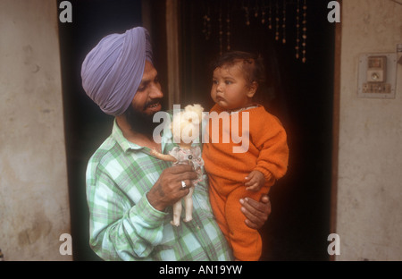Mann stand in der Tür halten Baby und Puppe, Punjab, Indien. Stockfoto