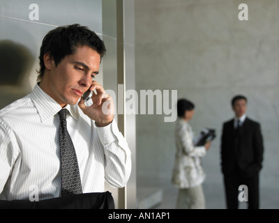 Drei Personen in einem Raum mit einem Mann im Vordergrund auf dem Handy Stockfoto