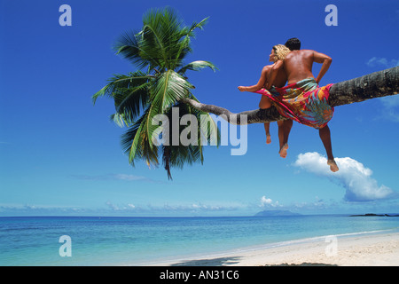 Paar sitzt auf Palme über Sandstrand Stockfoto