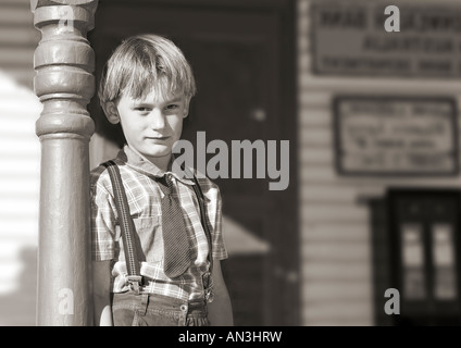 Silber-Gelatine-schwarz / weiß, eines kleinen Jungen in Krawatte und Hosenträger steht vor einem alten shop Stockfoto