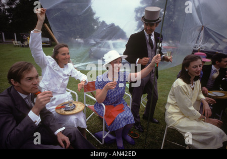 Picknick im Regen, Parkplatz schlechtes Wetter bei Royal Ascot Pferderennen. Mann trinkt Champagner. England Großbritannien 1985 1980er Jahre HOMER SYKES Stockfoto