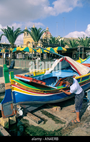 Man neigt dazu seine Luzzu Fischerboot am Hafen von Marsaxlokk, Malta gemalt. Stockfoto