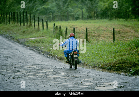 Ein Costa Rica Mann auf einem kleinen Motorrad fährt durch einen Regenwald Regen Regen Sturm in der Karibik Stockfoto