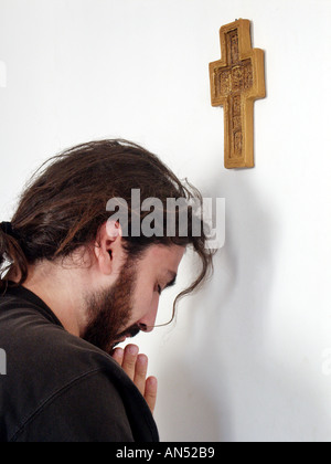 Beter unter Christian Cross an Wand Stockfoto