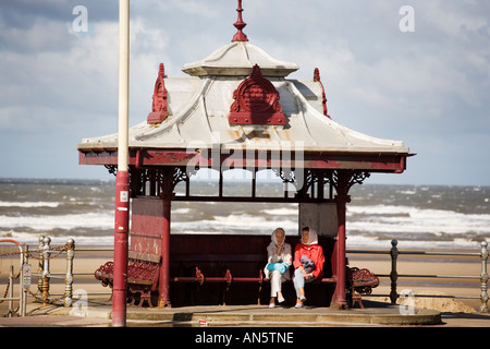 Zwei ältere Frauen sitzen in einem verblichenen viktorianischer Unterstand an der Promenade in Blackpool UK auf August Bank holiday Stockfoto