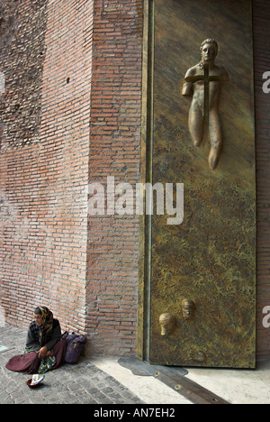 Eine Bettler Frau sitzt geschützt unter der massiven modernen Besetzung skulpturierten Messing Tür von der Kirche Santa Maria Degli Angeli Stockfoto