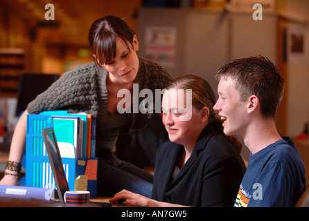 EIN TEENAGER-MÄDCHEN UND JUNGEN ARBEITEN AUF EINEM LAPTOPCOMPUTER UNTER ANLEITUNG VON EINEM LEHRER UK Stockfoto