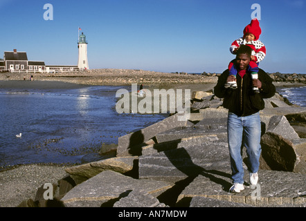 Vater trägt seinen Sohn auf seinen Schultern bei einem Spaziergang entlang einem Wellenbrecher an einem Wintertag Stockfoto