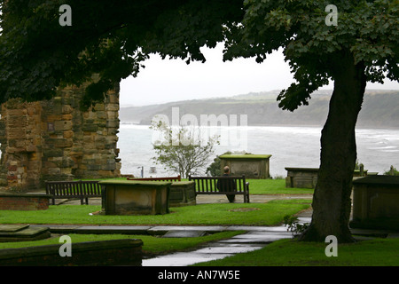 Mann sitzt auf Sitz im kirchlichen Friedhof mit Blick auf south Bay in Scarborough, North Yorkshire Stockfoto