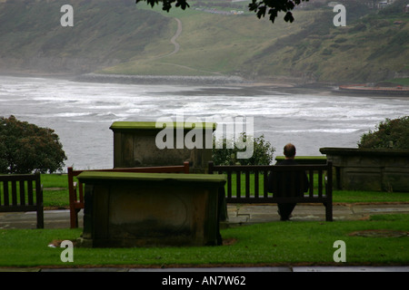 Mann sitzt auf Sitz im kirchlichen Friedhof mit Blick auf south Bay in Scarborough, North Yorkshire Stockfoto