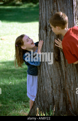 Ein Junge und ein Mädchen spielen Peek ein Boo um einen Baum Stockfoto