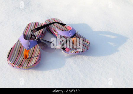 Sonnenbrillen und Strand Flip-Flops auf flachen Schnee auf einem sonnigen Winter Tagträumen von einer Flucht zu einem warmen Urlaub im Süden Stockfoto