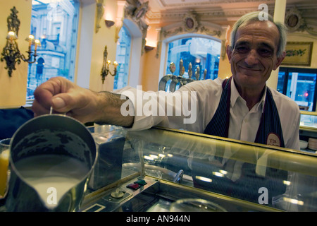 Ein Barkeeper serviert Milch auf eine Tasse Kaffee zum Frühstück in einem traditionellen spanischen Café in Granada, Spanien. Stockfoto