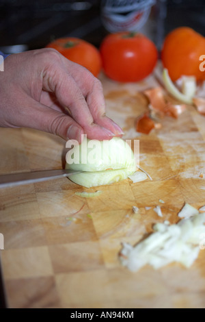 Mans Hand schneiden Zwiebeln auf Holzblock mit Tomaten im Hintergrund Stockfoto