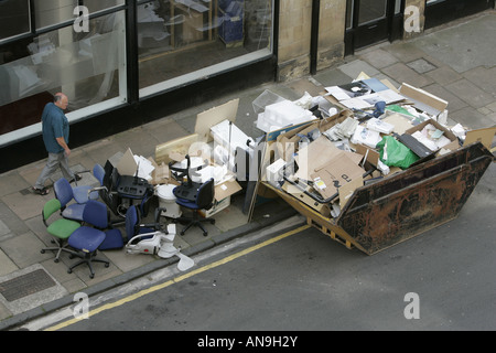 EIN MANN GEHT EINE SKIP VOLL UND ÜBER MIT AUSRANGIERTEN BÜROMASCHINEN FLIEßT. Stockfoto