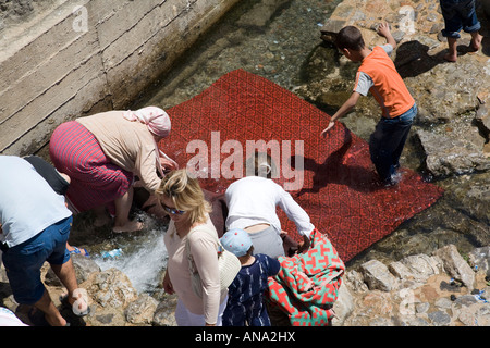 Frauen und Kinder waschen Teppiche und decken in einem öffentlichen Waschplatz am Fluss, Chefchaouen, Marokko Stockfoto