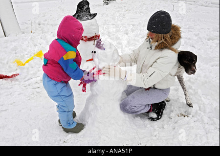 Kinder bauen Schneemann mit Mutter nach einem Winter Schneefall Stockfoto