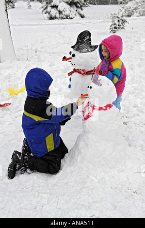 Kinder bauen Schneemann mit Mutter nach einem Winter Schneefall Stockfoto