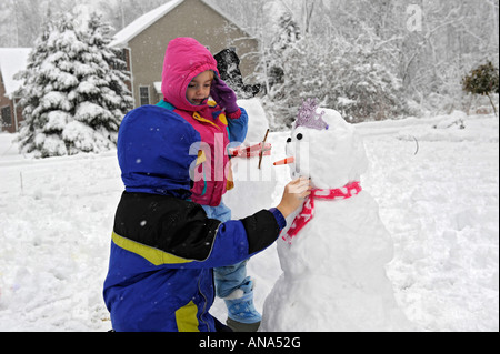 Kinder bauen Schneemann mit Mutter nach einem Winter Schneefall Stockfoto